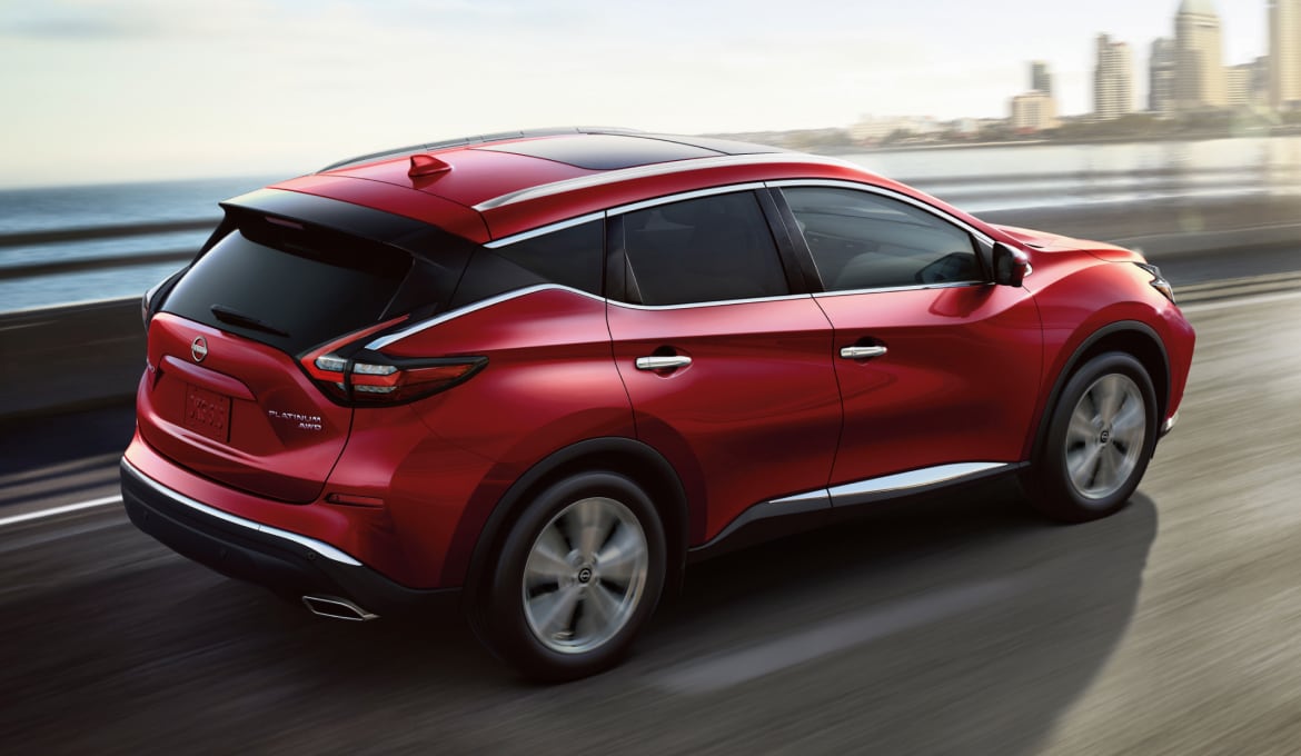 Red 2024 Nissan Murano driving fast on a bridge over water with a city in the background