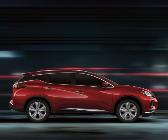 Side profile of a red 2024 Nissan Murano driving fast on a dark street with a blurred background