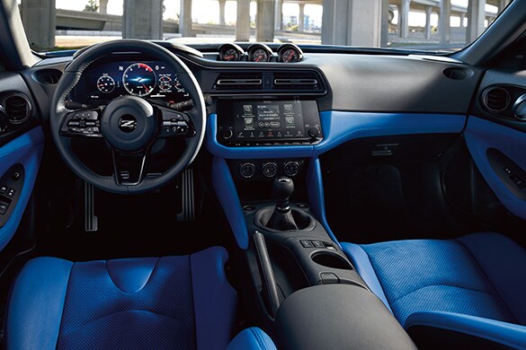 2023 Nissan Z driver oriented cockpit in blue showing gear shifter, gauges, and digital displays.