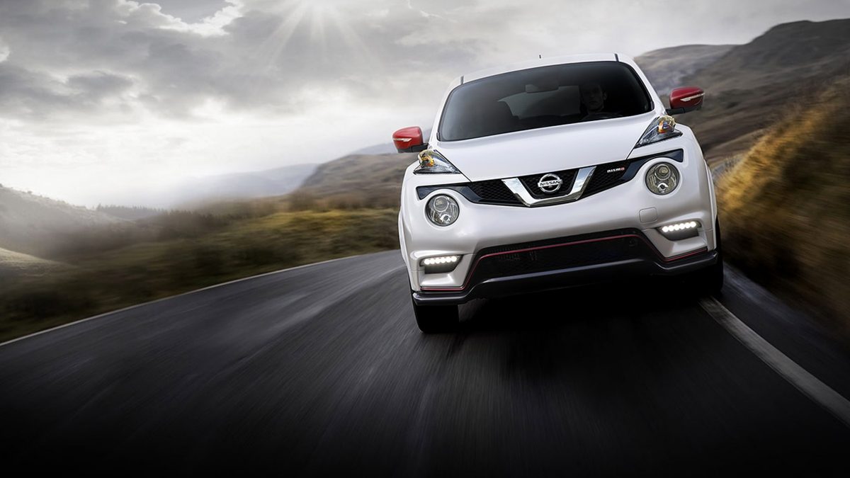 A front view of a white Nissan JUKE NISMO with red mirror accents driving on a country road