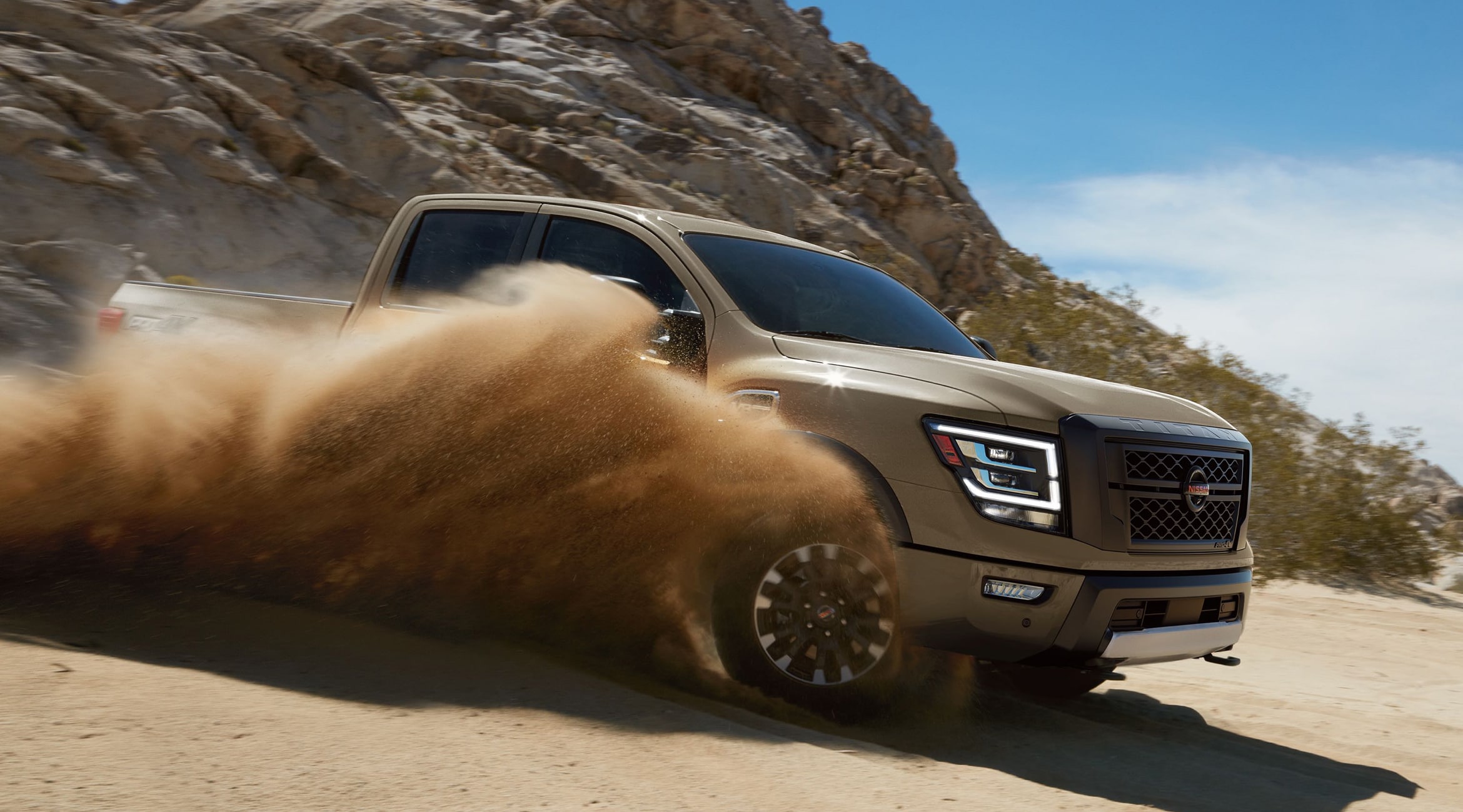 A brown Nissan Titan Truck driving in the sand