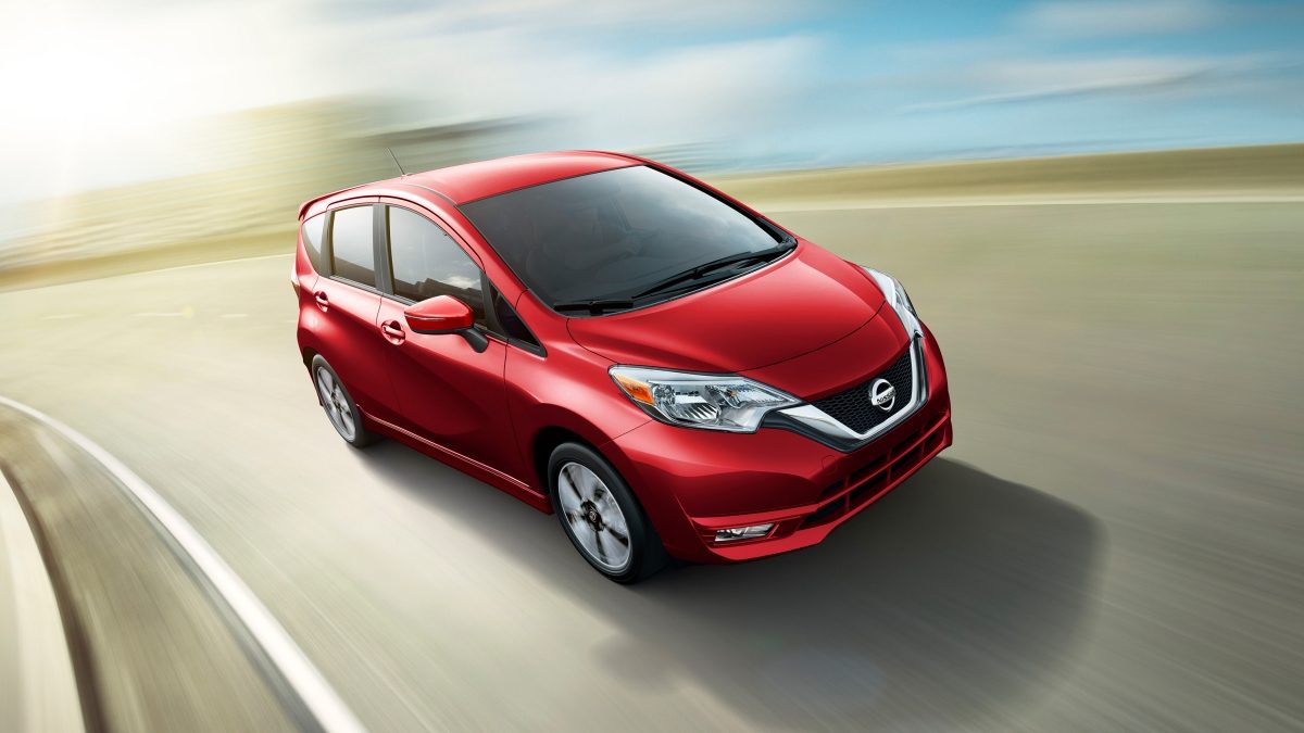 A red Nissan Versa Note driving on a coastal freeway