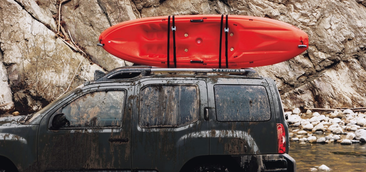 Red kayak strapped onto roof of Nissan Xterra