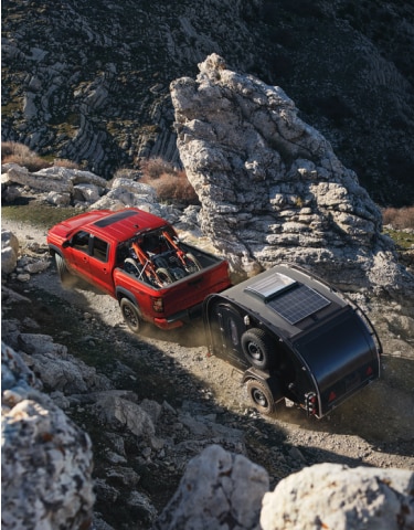 Red 2024 Nissan Frontier towing trailer up rocky landscape