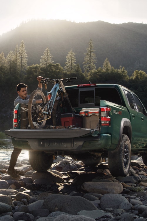 2024 Nissan Frontier bed being loaded with gear and a bike in the mountains