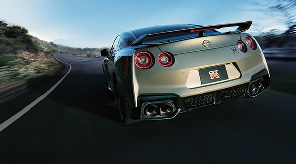 2024 Nissan GT-R in Bayside Blue driving toward the sun on an open road.