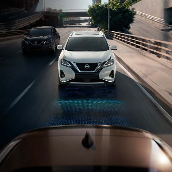 View from a vehicle in front of a white 2024 Nissan Murano driving. A blue illustration is on the road between the vehicles to demonstrate Intelligent Cruise Control 