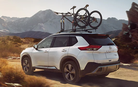 2023 Nissan Rogue in pearl white on mountain road and bikes on roof rack.