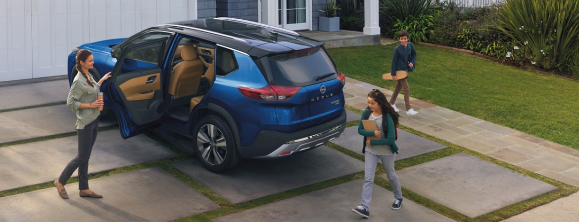 2023 Nissan Rogue in a driveway with door open and family about to get in.
