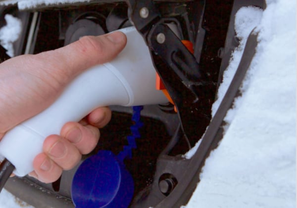 Hand plugging in Nissan EV covered in snow